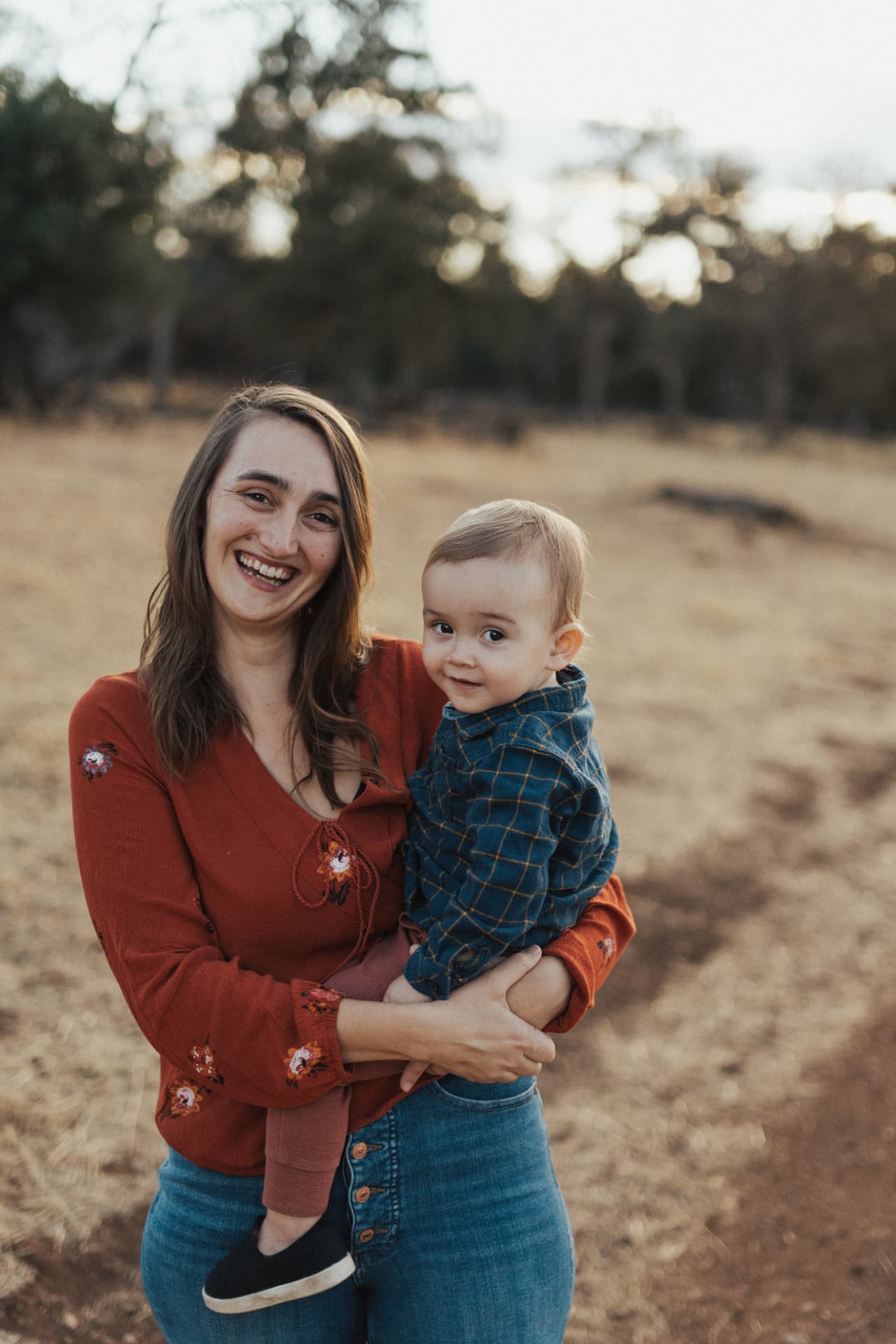 Nora smiling and holding her toddler in a sunlit field